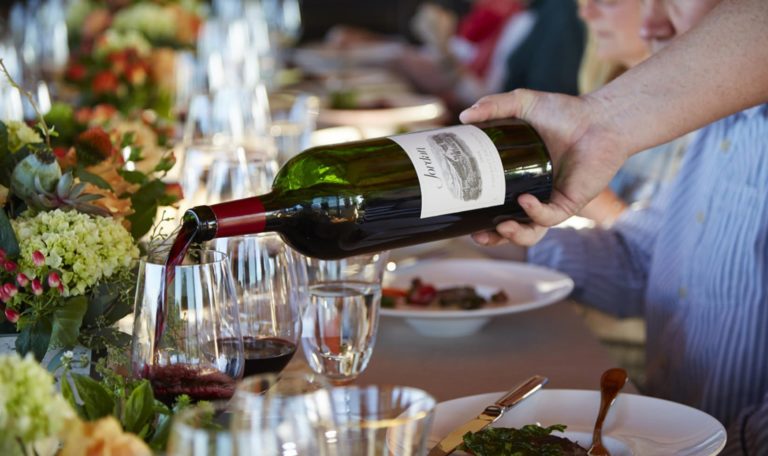 magnum of Jordan Winery Cabernet being poured into a glass as guests are seated at a table at a Sunset Supper Vineyard Dinner