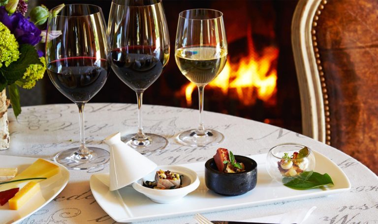 wine flight with food bite pairings on a table in the Jordan Winery dining room with fire burning in fireplace in background