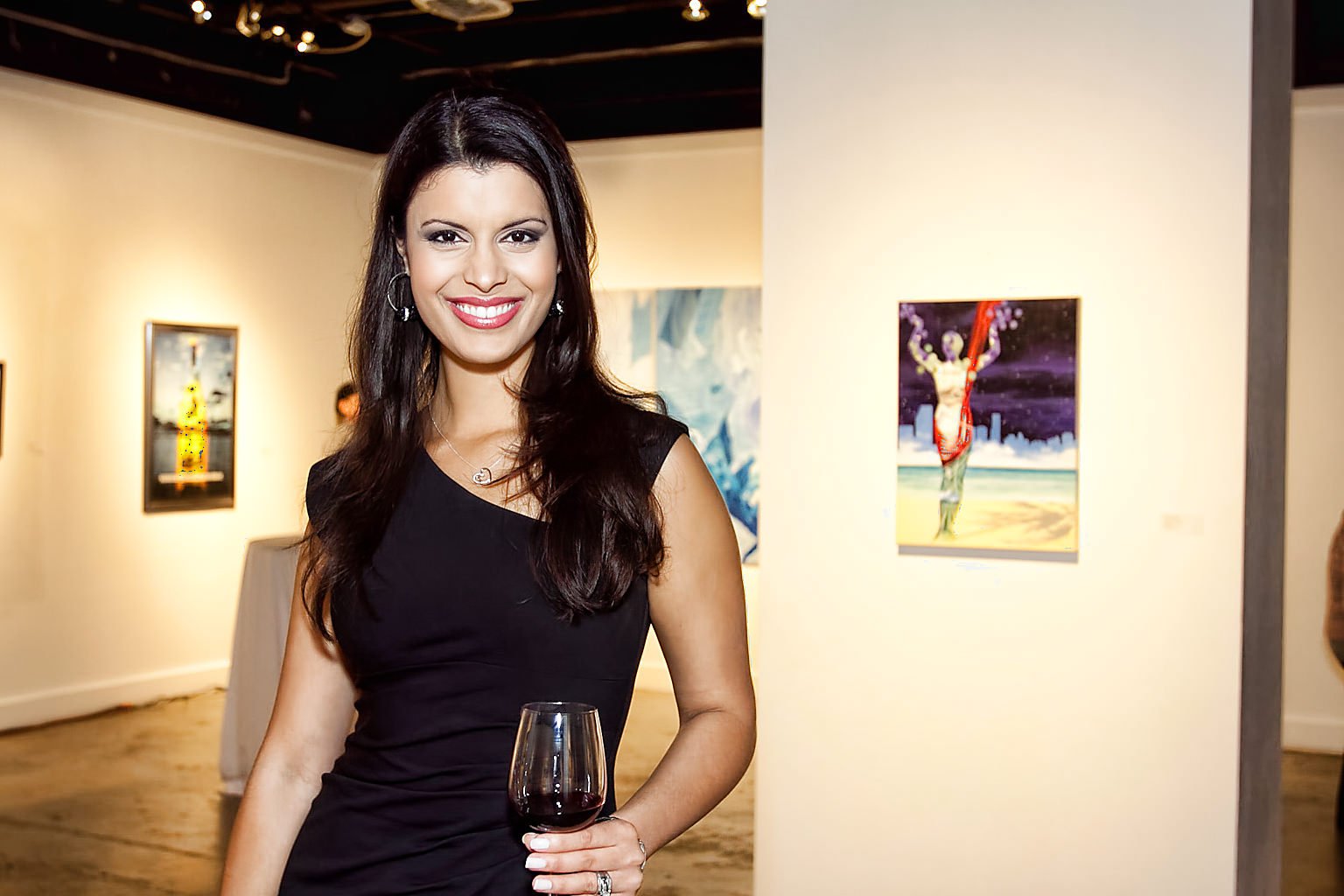 Woman smiling and standing in an art gallery holding a glass of red wine