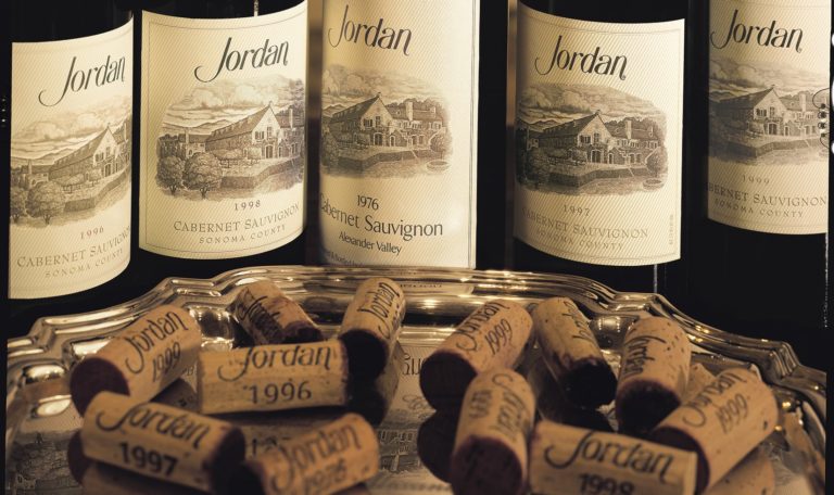 different older vintages of Jordan Winery Cabernet lined up in the background with a silver tray full of different vintages of Jordan Winery corks on it in the foreground