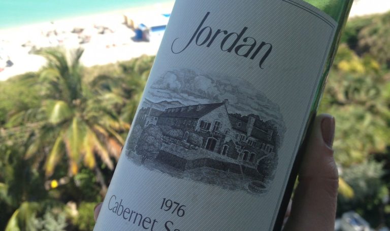 Close up of a bottle of 1976 Jordan Winery Cabernet with a beach setting in the background