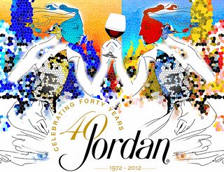 A piece of art from the 4 on 4 Jordan Winery art competition. It features 2 mirrored women's profiles in line work holding the same glass of red wine. They are loosely filled in with blue and orange pixelated hexagons. Centered below is Jordan's 40 year celebration logo.