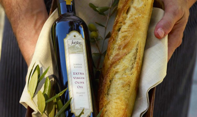 2011 Jordan Estate Extra Virgin Olive Oil in a basket with fresh bread and olive branches.