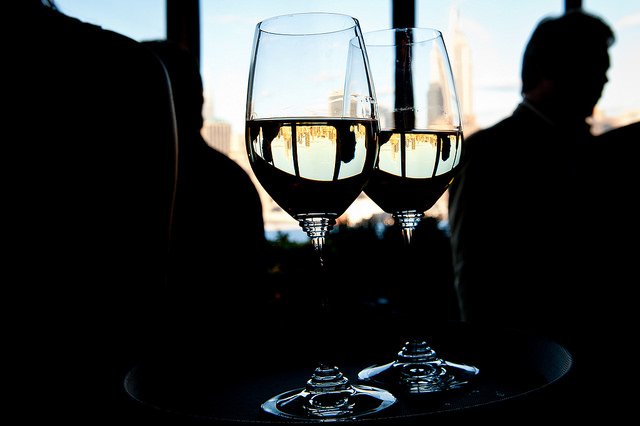 Two glasses of white wine with silhouettes of people in the background