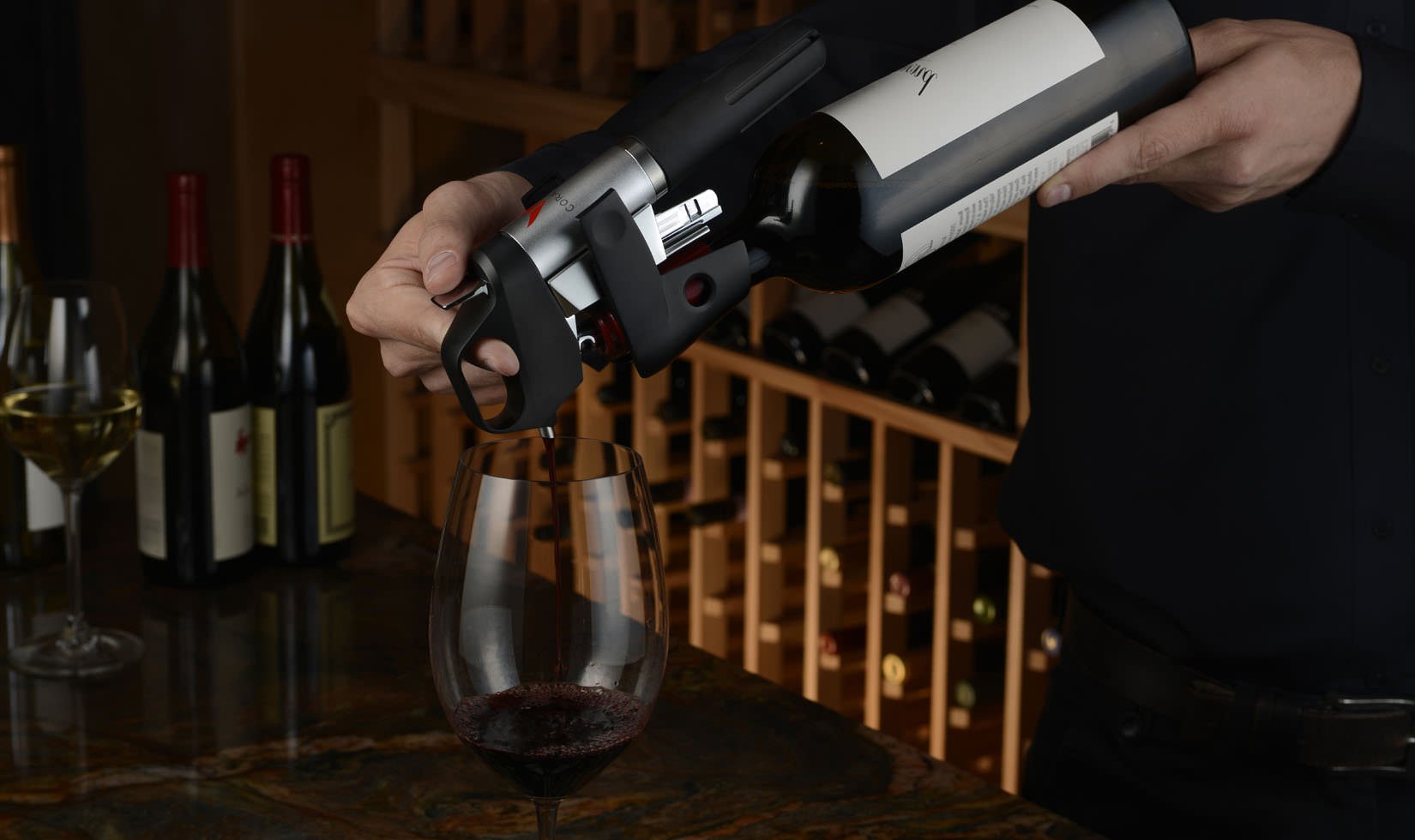 close up of a hand holding a Coravin pouring red wine into a wine glass