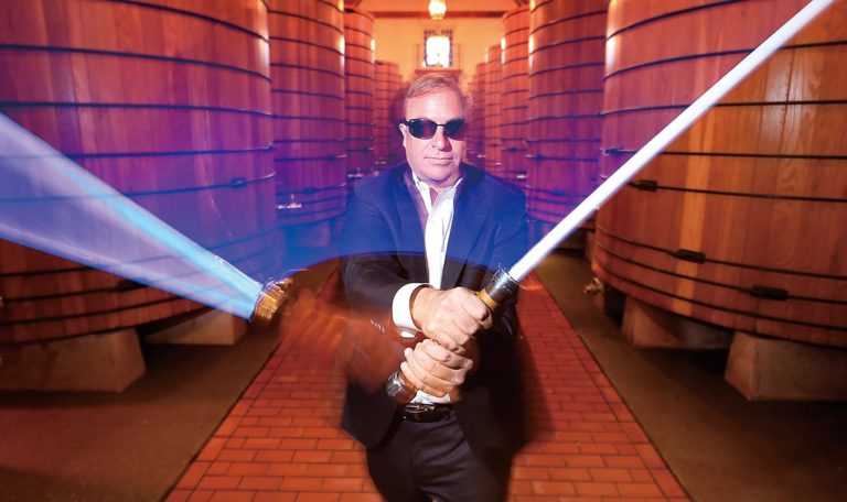 John Jordan, CEO and proprietor of Jordan Winery in the large oak tank room at Jordan Winery in a suit with sunglasses swinging a lightsaber