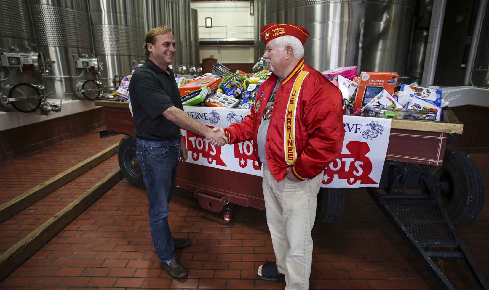 John Jordan, CEO and proprietor of Jordan Winery shaking hands with a US Marine Crop member in front of a sleigh full of toys to be donated to Toys for Tots