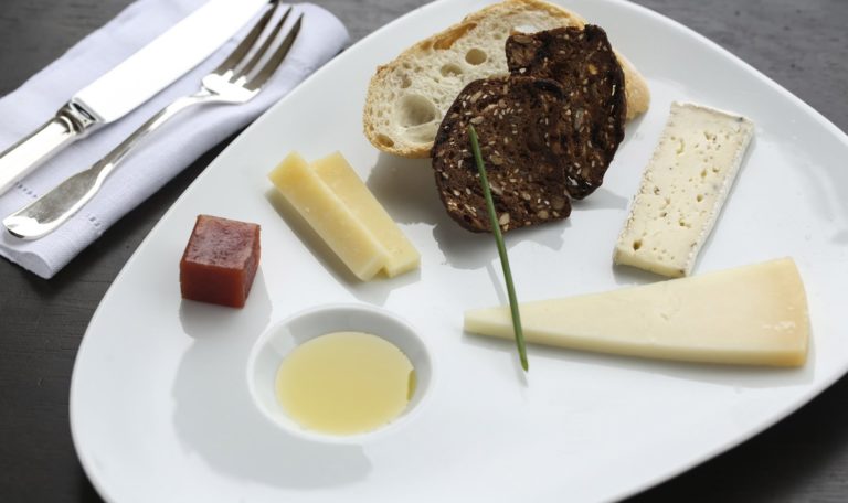 close up of a cheese plate with three cheeses, olive oil, and quince paste