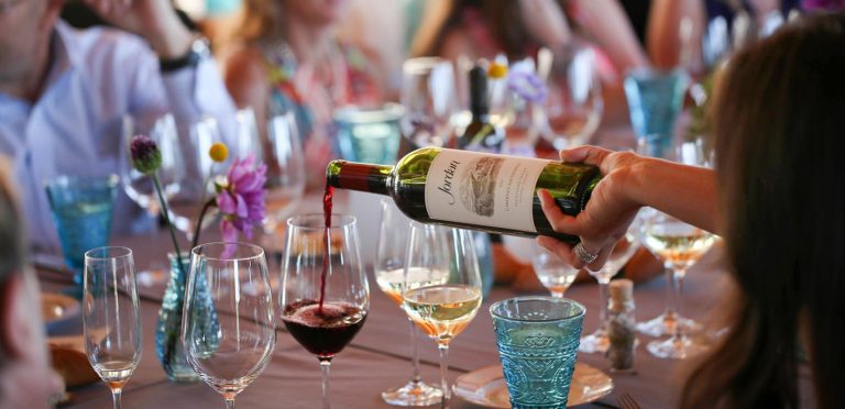 hand pouring Jordan Winery Cabernet into a glass at a Sunset Supper event at Jordan Winery with guests seated at table in the background