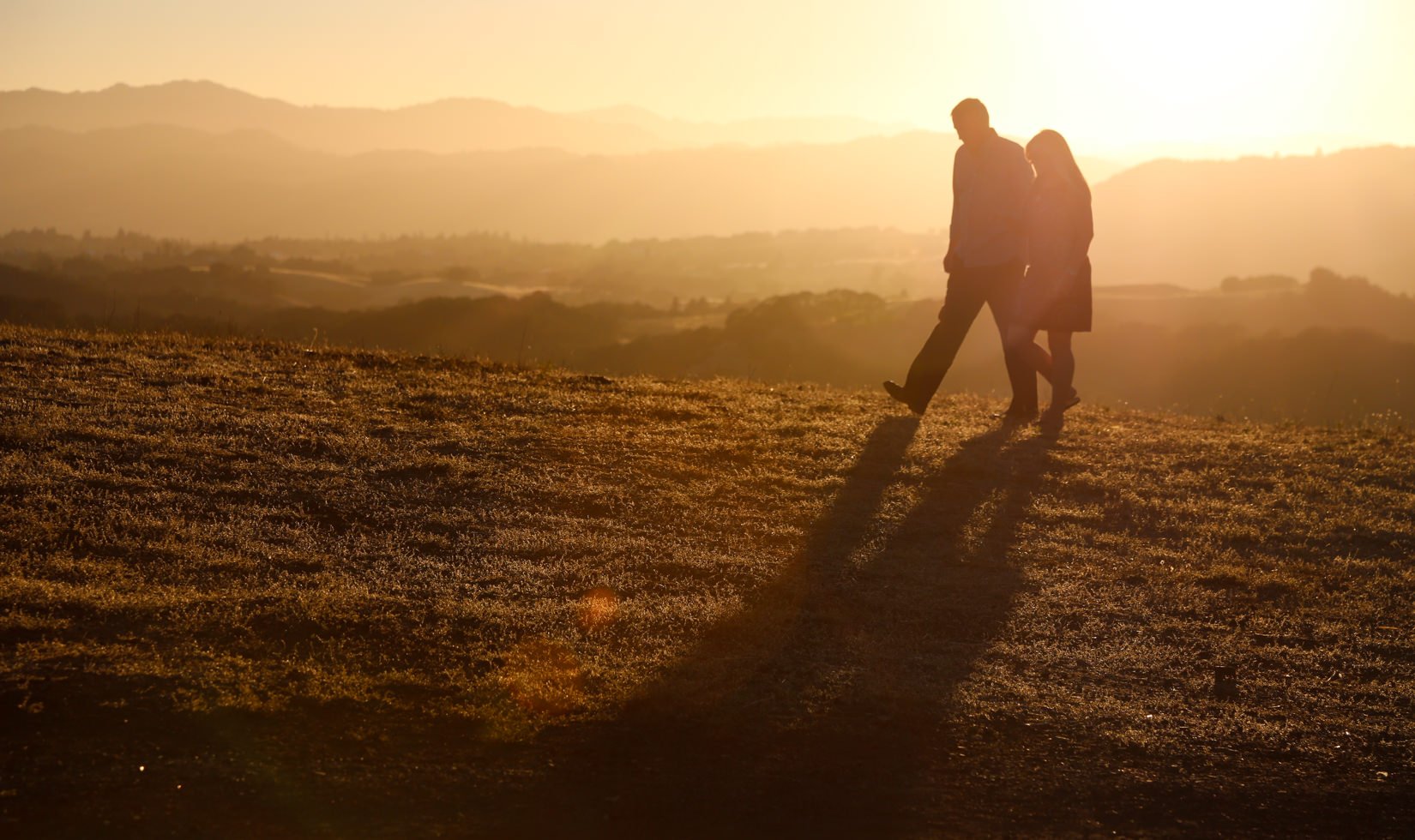 A couple walks hand-in-hand with the sunset in the background.