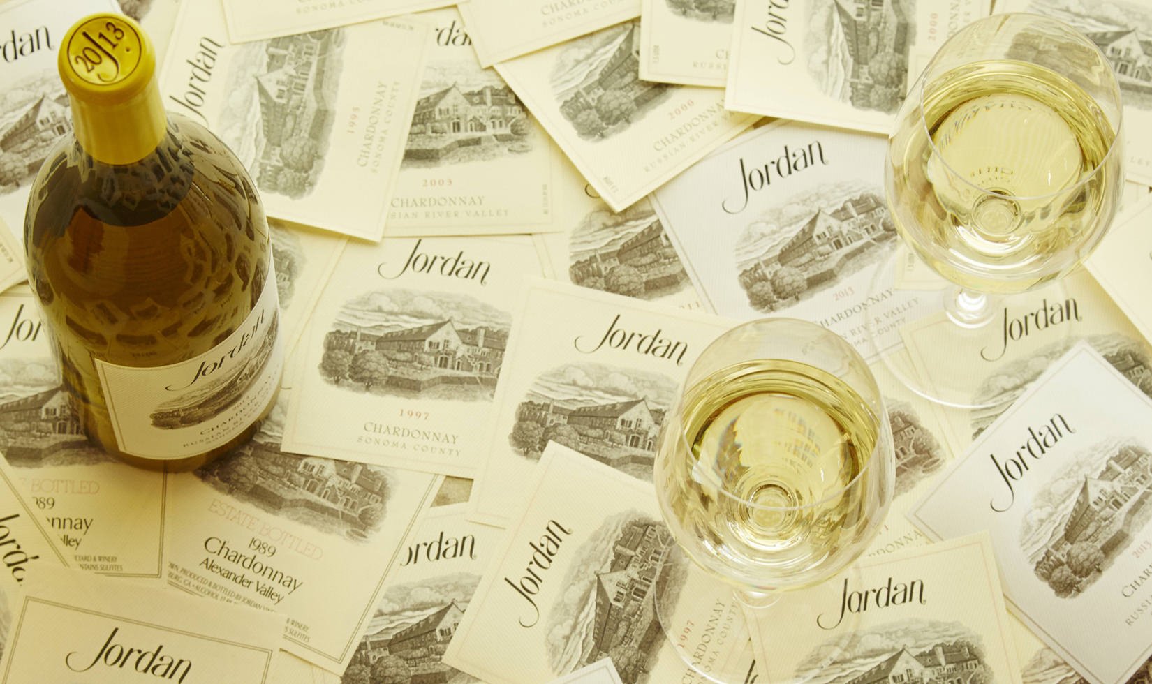 a bottle of Jordan Winery Chardonnay with two poured glasses of wine on top of wine labels