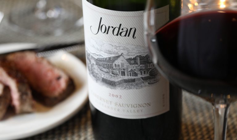 sliced steak on a plate next to a bottle of Jordan Winery 2002 Cabernet