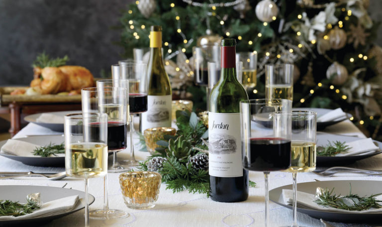 table setting for a Holiday dining experience with Jordan Winery Cabernet and Chardonnay, festive pinecone centerpieces, and a festive holiday tree in the background