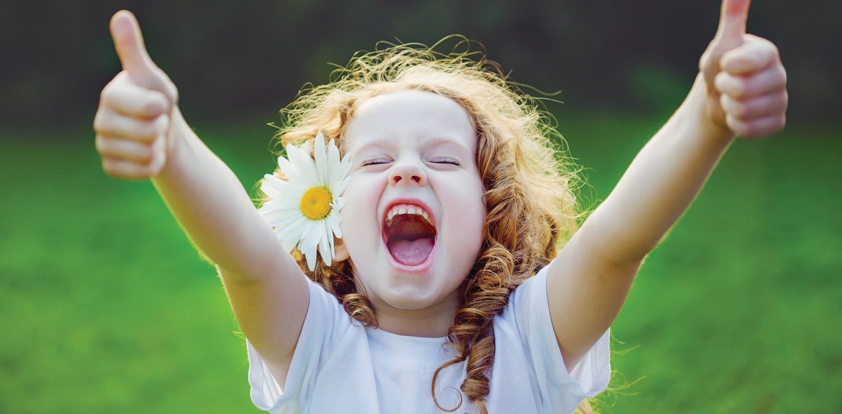 little girl smiling at camera with thumbs up and a large daisy tucked behind her ear