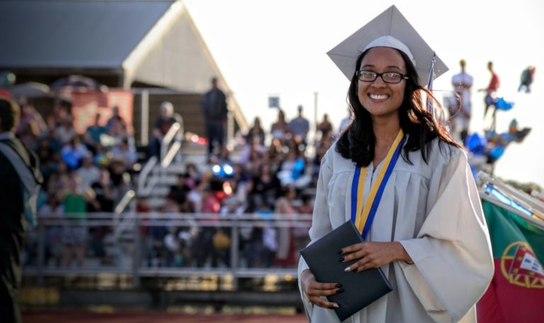 Student smiling at camera in a cap and gown at a graduation ceremony