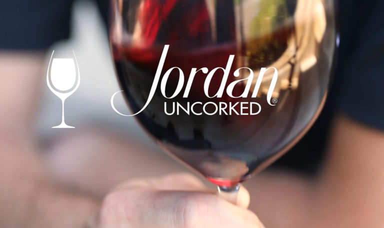 still from a video made by Jordan Winery featuring a close up of a hand holding a glass of Jordan Winery Cabernet with image text: "Jordan Uncorked"