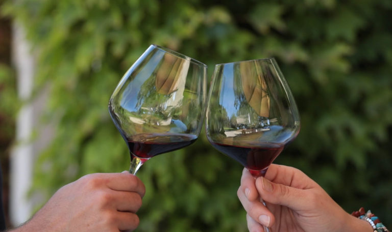hands holding two wine glasses toasting with pours of red wine