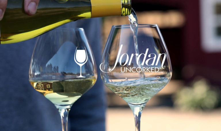 still from a video made by Jordan Winery featuring a close up of a hand pouring Jordan Winery Chardonnay into a glass next to a poured glass of Chardonnay with image text: "Jordan Uncorked"