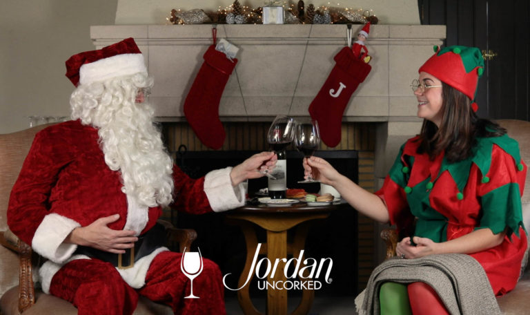 still from a video made by Jordan Winery featuring John Duckett and Maggie Kruse of Jordan Winery dressed as Santa Claus and a holiday elf toasting with glasses of Jordan Winery Cabernet with image text: "Jordan Uncorked"