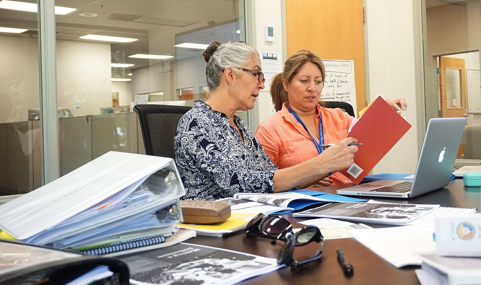 Two women sitting at a table in front of a laptop discussing the TALLK program through the John Jordan Foundation