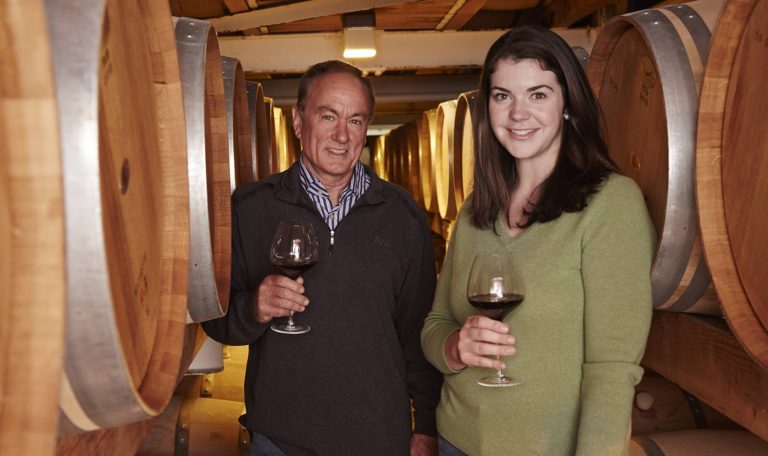 Rob Davis, former winemaker at Jordan Winery and Maggie Kruse, current winemaker at Jordan Winery standing in the Jordan Winery barrel room with poured glasses of Cabernet