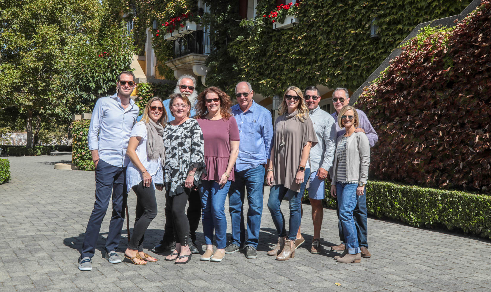 A group of guests at Jordan Winery in wine country casual attire. Most are wearing sunglasses, nice jeans, button down shirts, and/or flowy blouses.