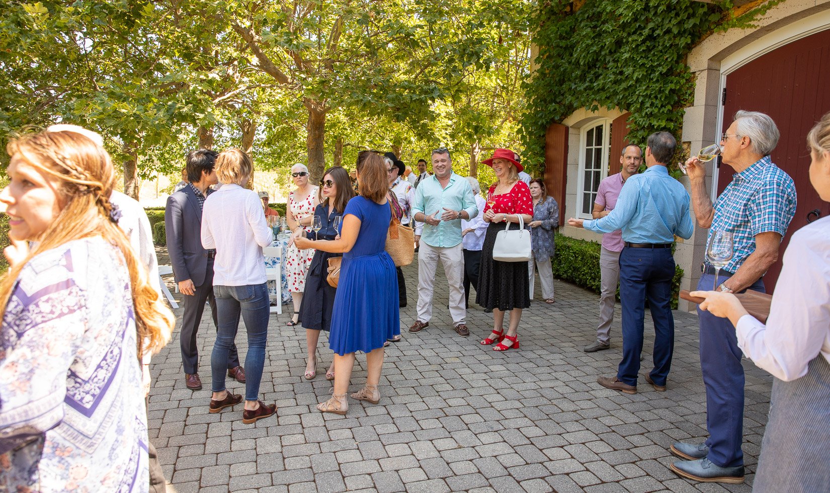 Guests socializing in the Jordan Winery courtyard. Most men are in jeans or slacks and a button down shirt. The women are in knee length dresses or nice pants.