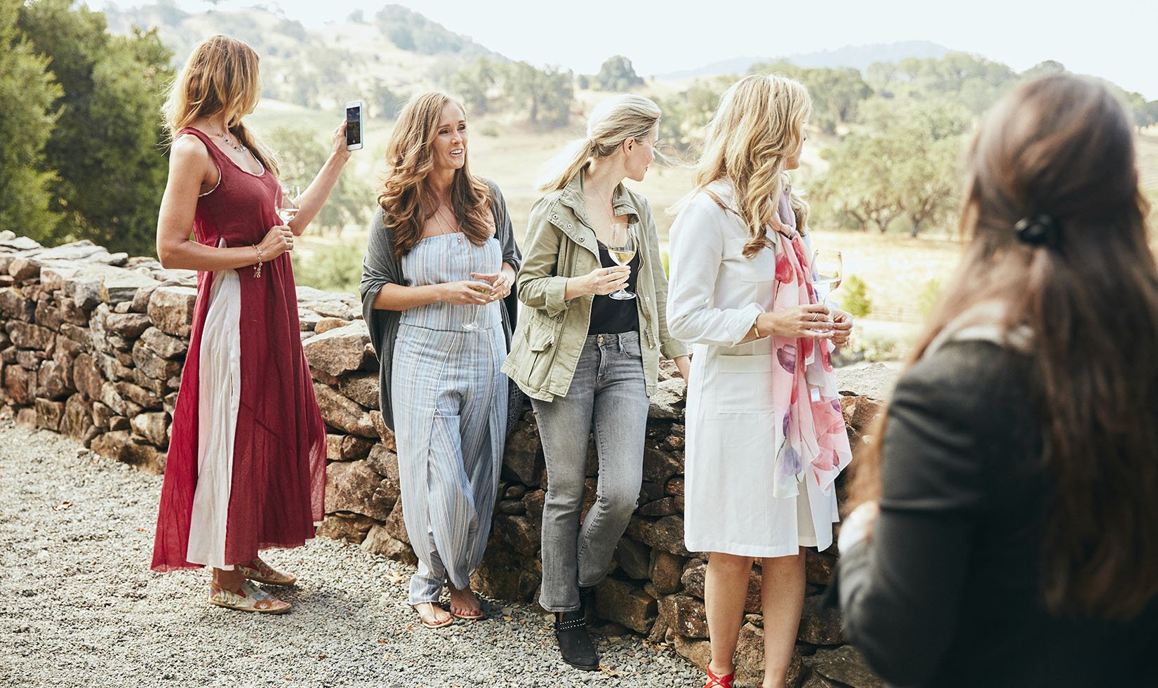 Four women leaning on a rock wall overlooking the Garden at Jordan Winery in wine country casual attire.