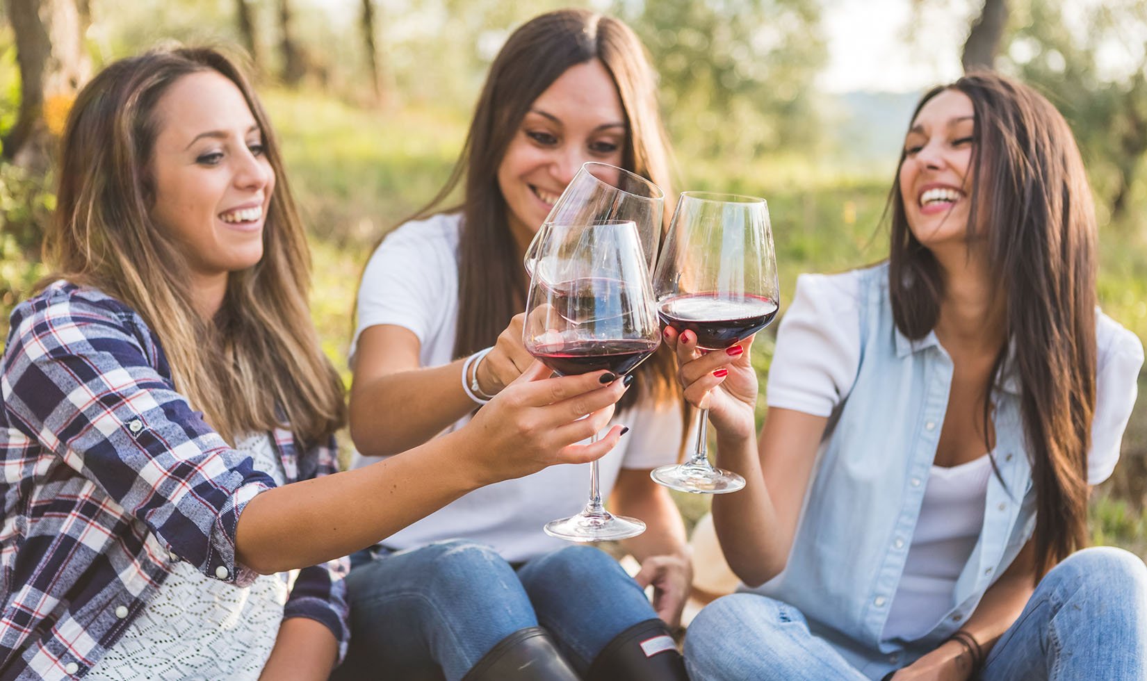 3 women toasting with glasses of red wine in wine country casual attire.