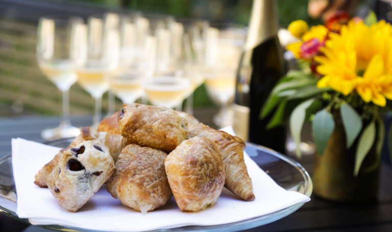 Plate of pastries with wine glasses and flowers in the background