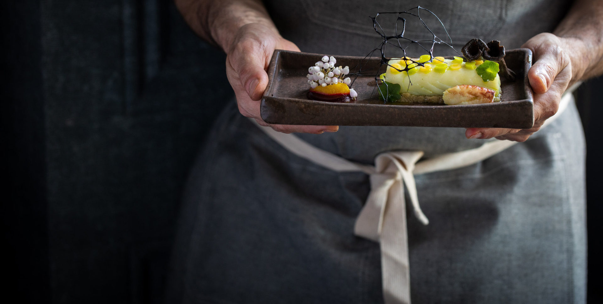 Person wearing an apron holding a dish of gourmet food