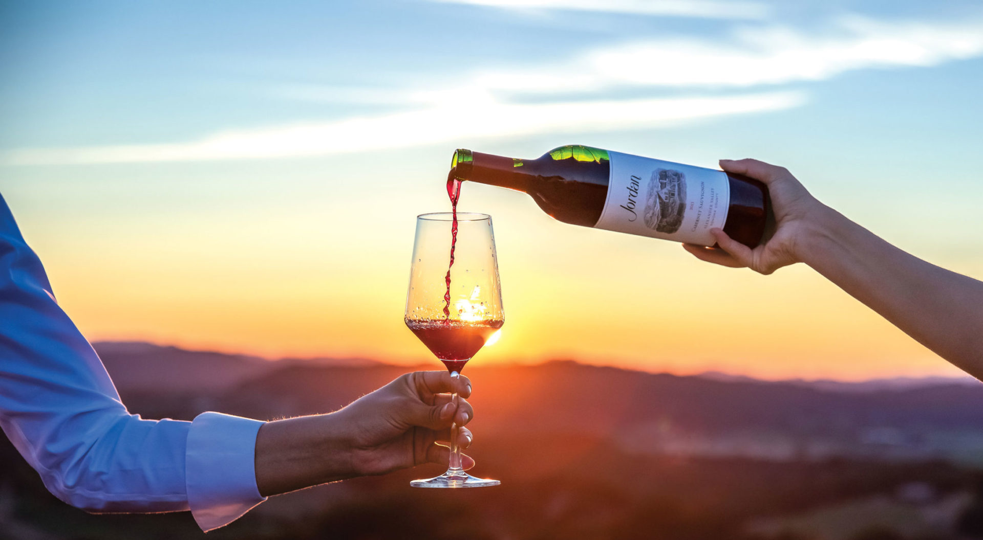 Hand pouring Jordan Cabernet Sauvignon in front of a sunset