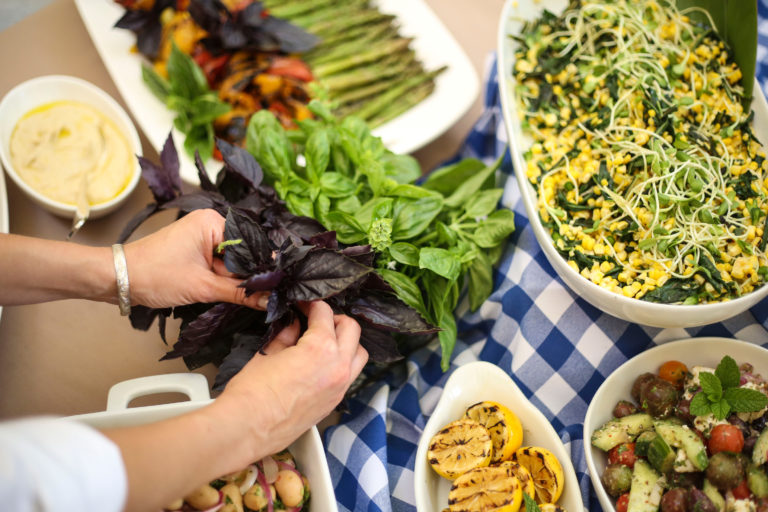 Hands holding basil leaves next to serving dishes filled with food