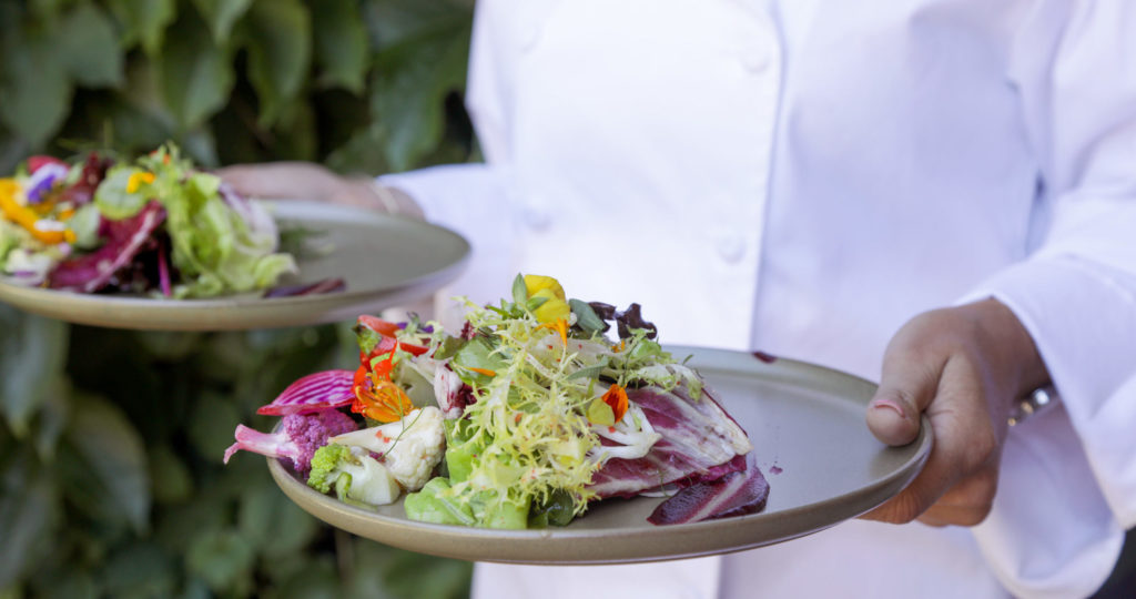 Chef walking outside with two plates of salad