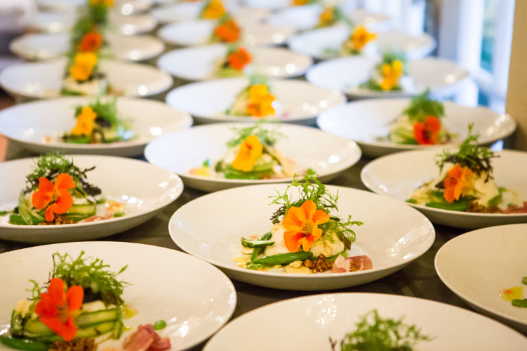 table filled with entree dishes with salad greens and orange edible flowers