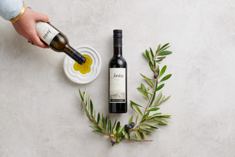 Bottles of Jordan Estate Extra Virgin Olive Oil and a olive branch