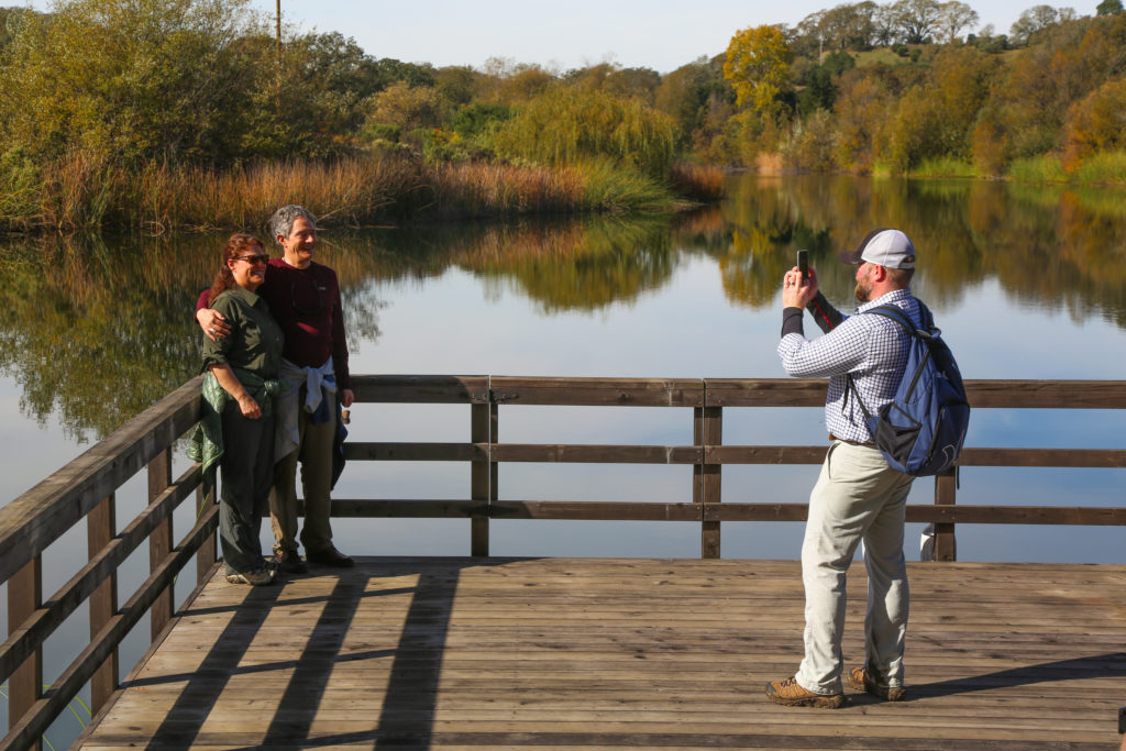 photographer taking image of couple next to vineyard lake