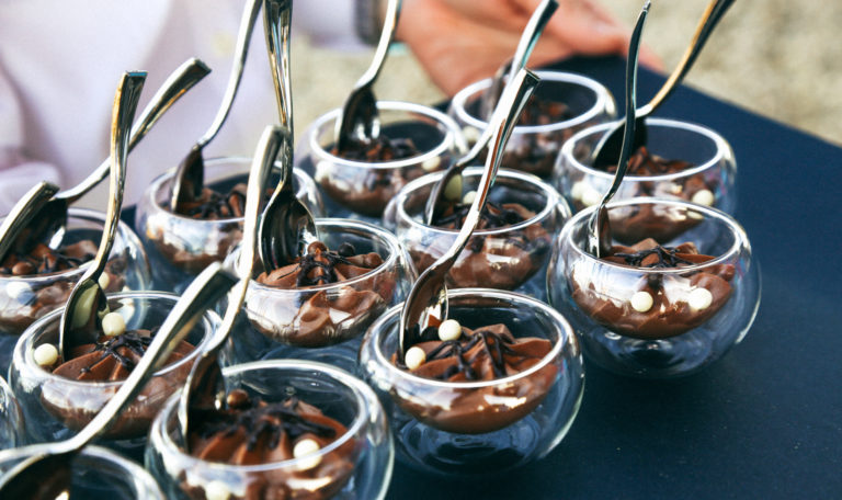 Mini bowls of chocolate mousse, each with a silver spoon, served on a black tray.
