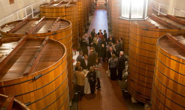 Guests enjoying a wine tasting event surrounded by gigantic tun barrels in Jordan's Winery cellars.