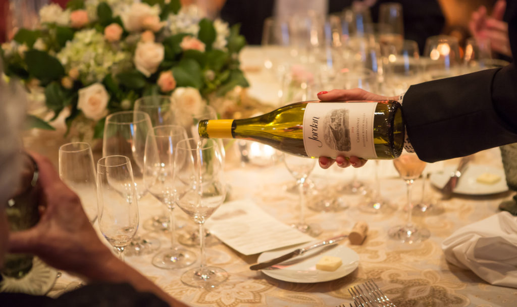 A waiter's right hand pours Jordan's Chardonnay into a glass on a formally set table.