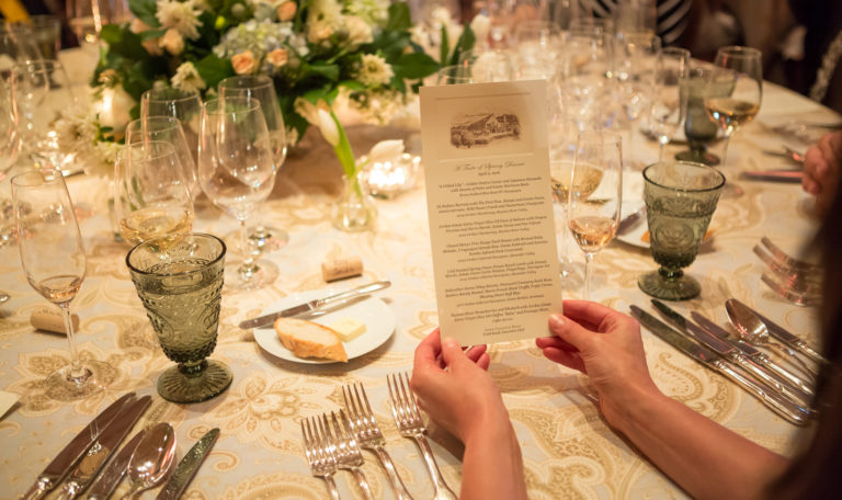 Looking over the shoulder of a woman holding Jordan Winery's Spring Dinner tasting menu at a formally set table.