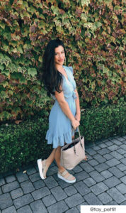 Woman wearing blue wrap dress in front of ivy. She has beige platform sandals and bag.