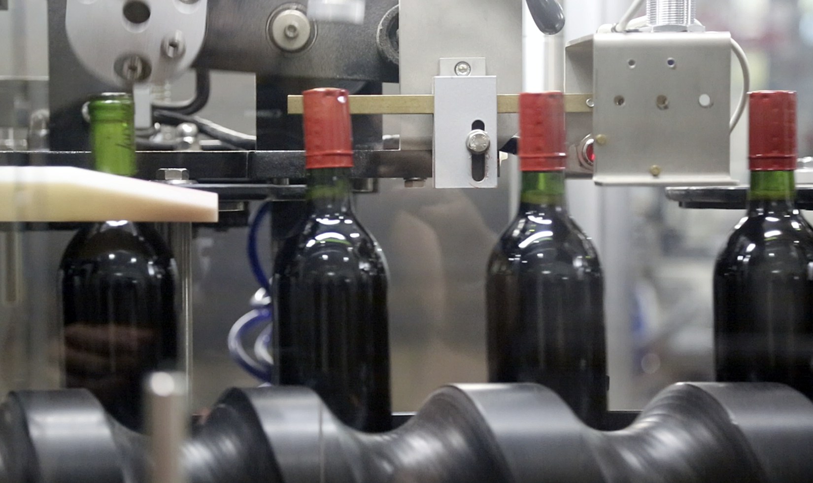 4 bottles of red wine in a capsulator being corked and sealed.