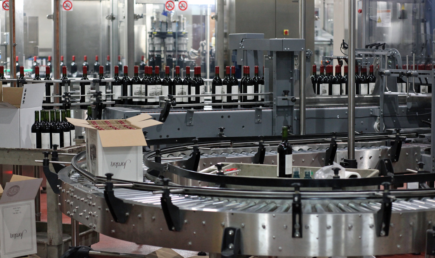 A freshly packed case of red wine goes down the conveyor as bottles line up in the background.