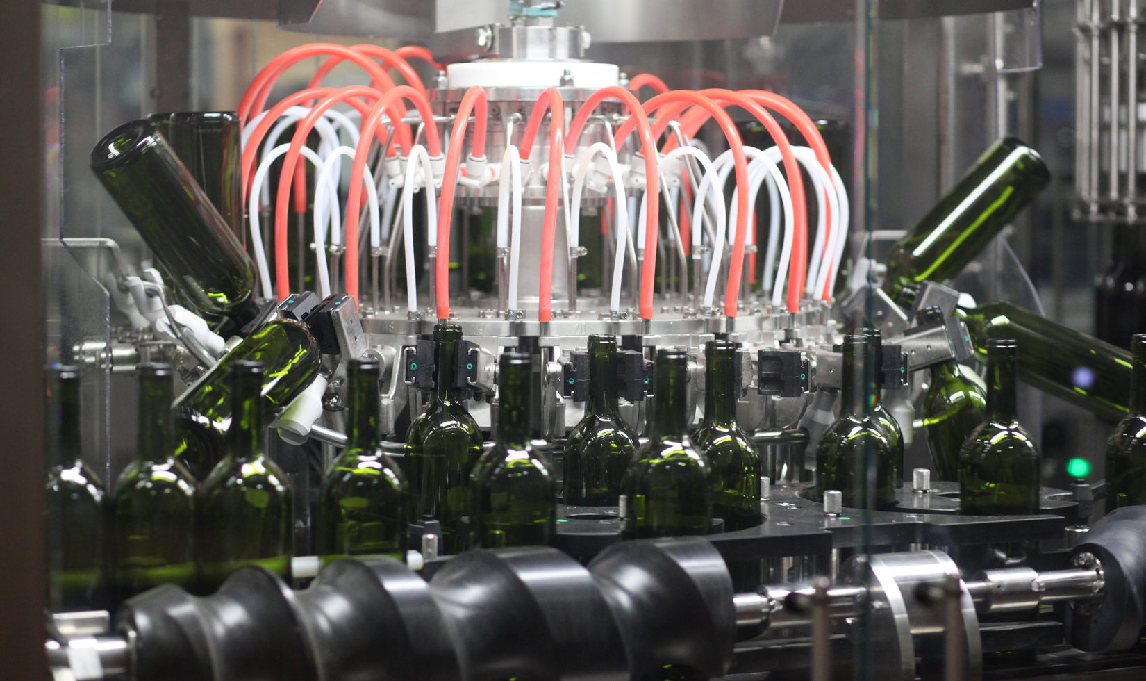Unlabeled green wine bottles in Jordan Winery's nitrogen sparging machine. It's cylindrical with red and white tubes filling the surrounding bottles.