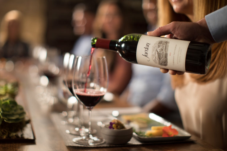 Red wine poured into a glass with food pairings on a table