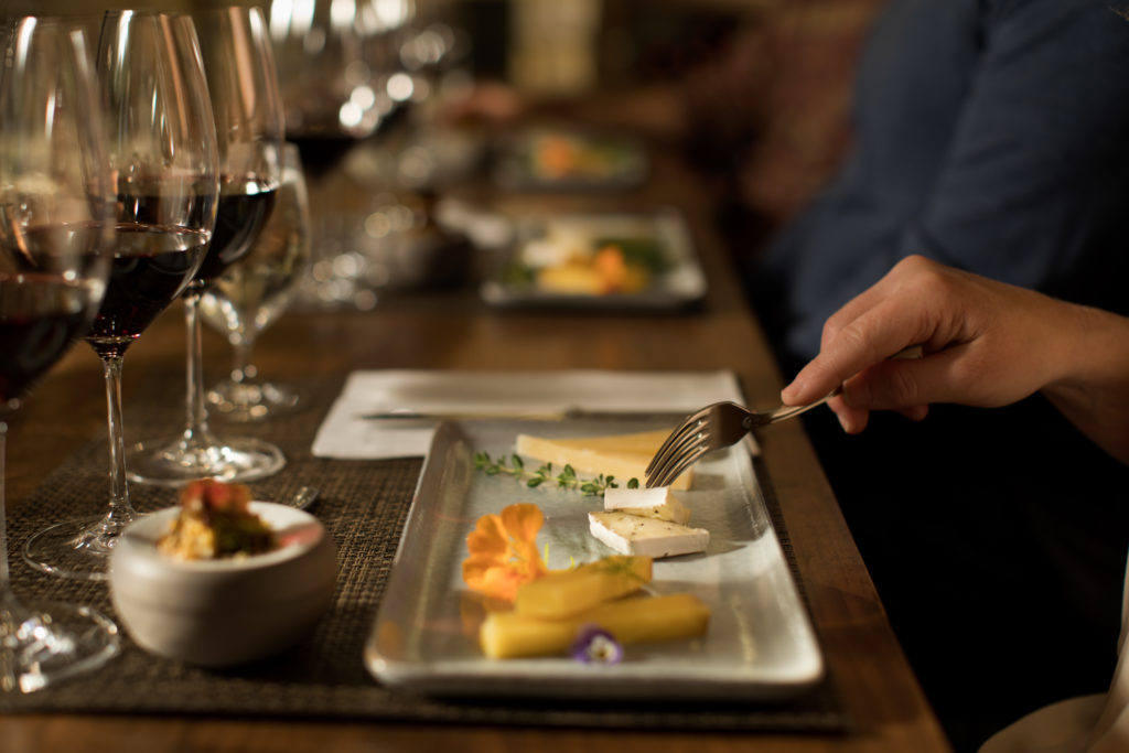 person holding a fork near cheese plate with red wine