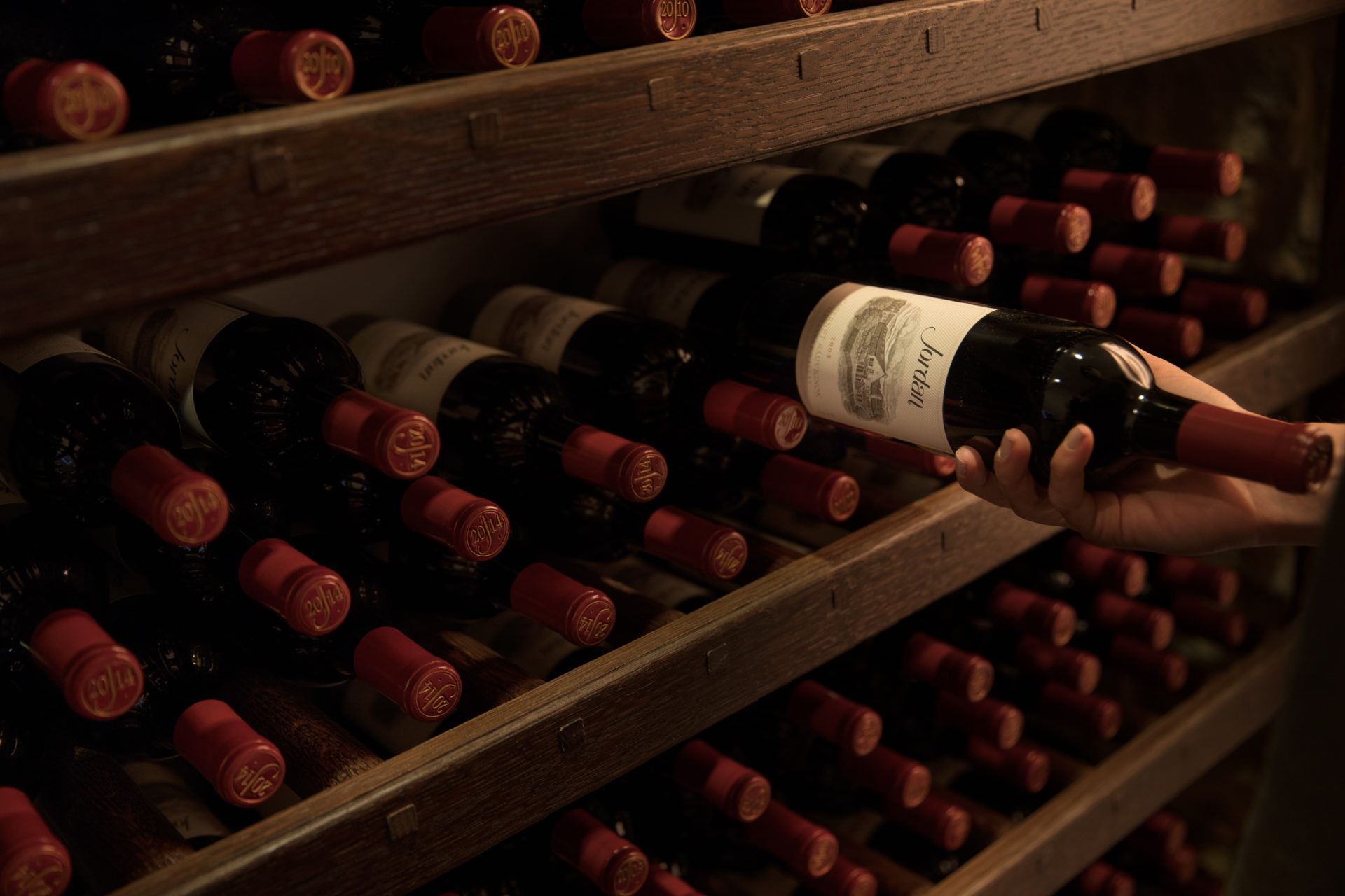 Hand grabbing a bottle of cabernet sauvignon from a shelf lined with wine bottles