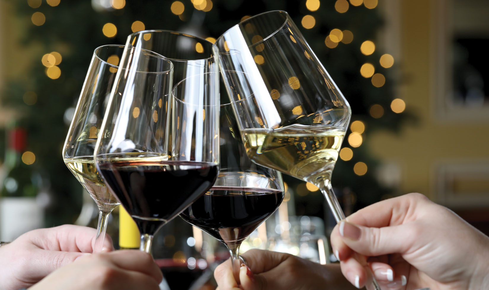 wine glasses filled with red and white wine toasting with a Christmas tree in the background