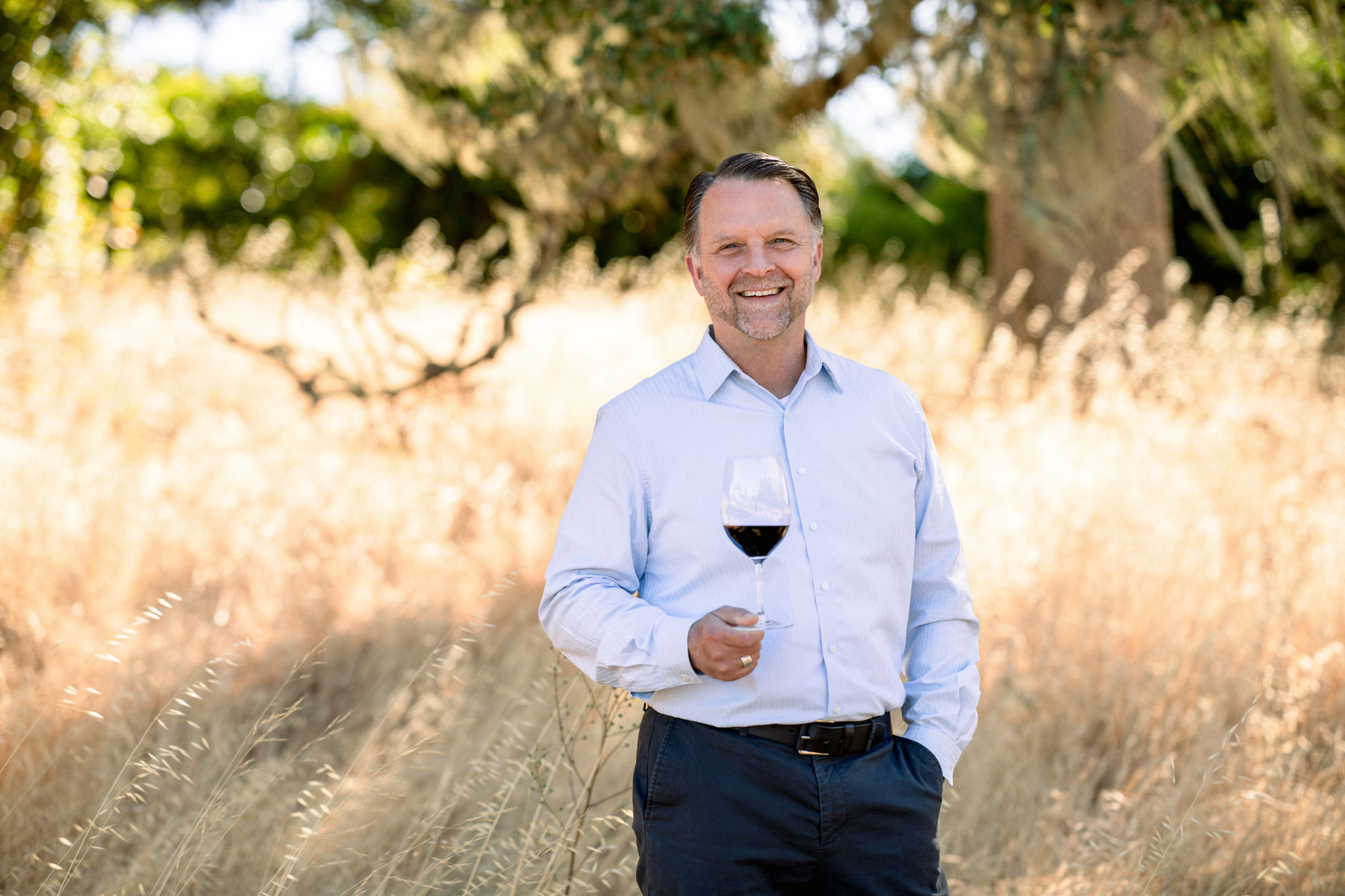 one man standing in business attire with glass of cabernet in hand